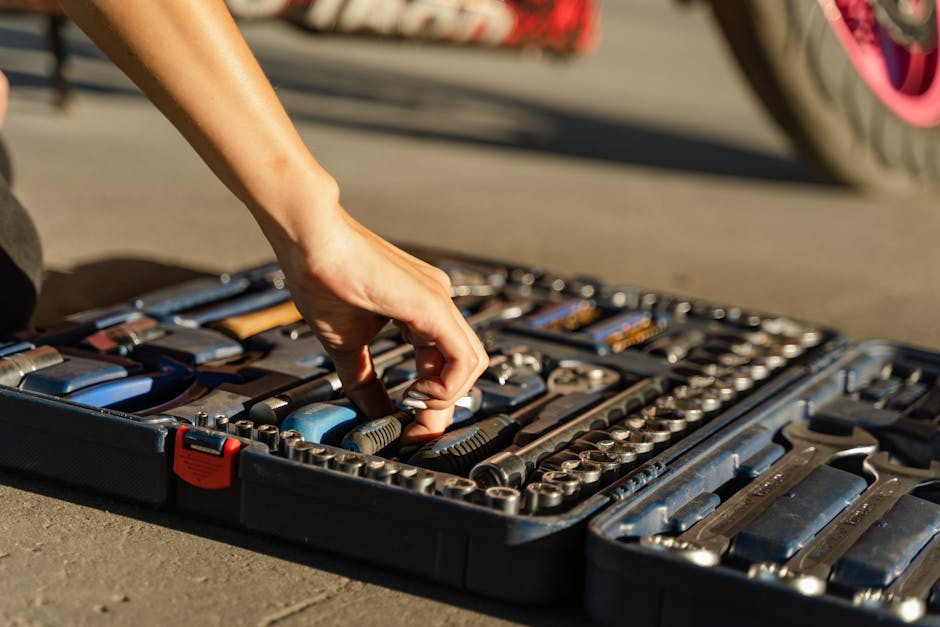 Close-up of a hand selecting a tool from an organized toolbox in sunlight.